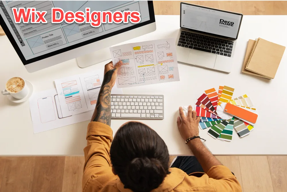 Overhead view of a designer comparing printed wireframes and colour swatches beside a monitor showing a page layout, captioned Wix Designers